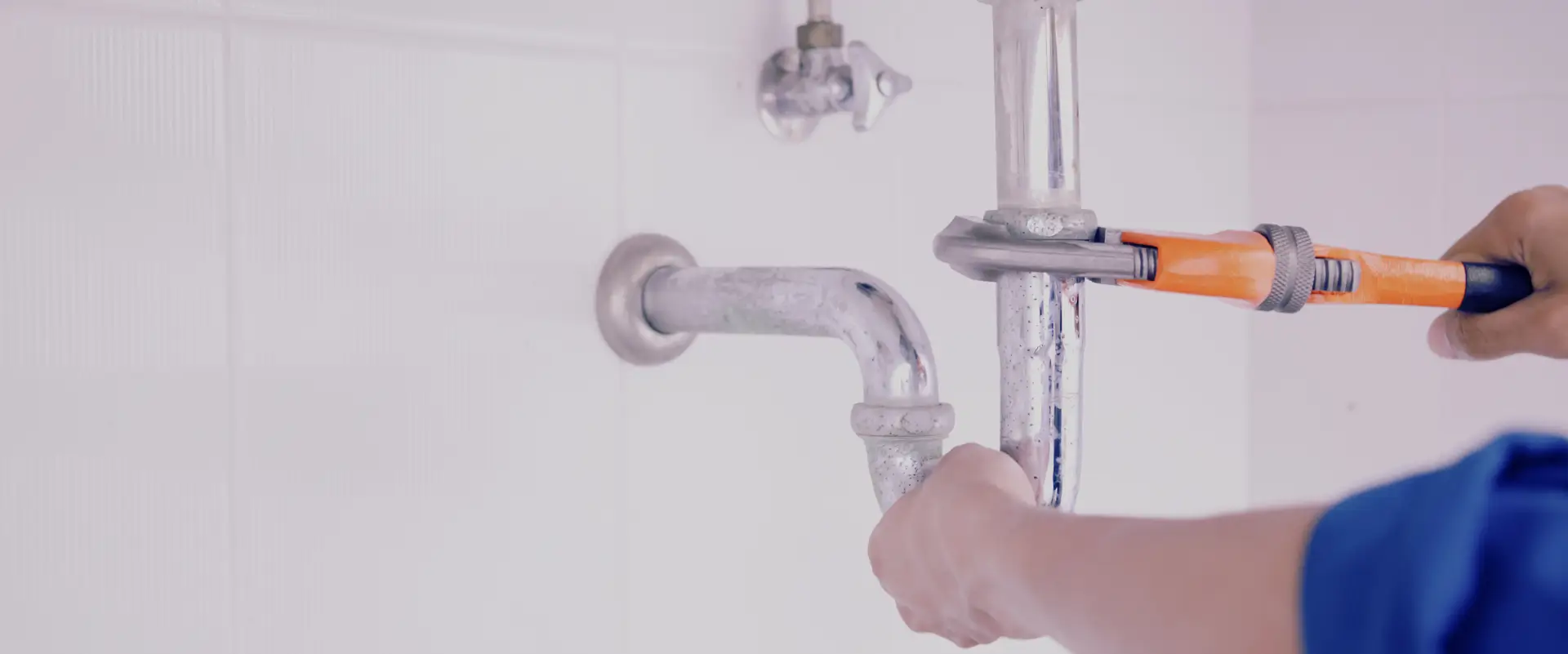Plumber adjusting a sink pipe with a wrench